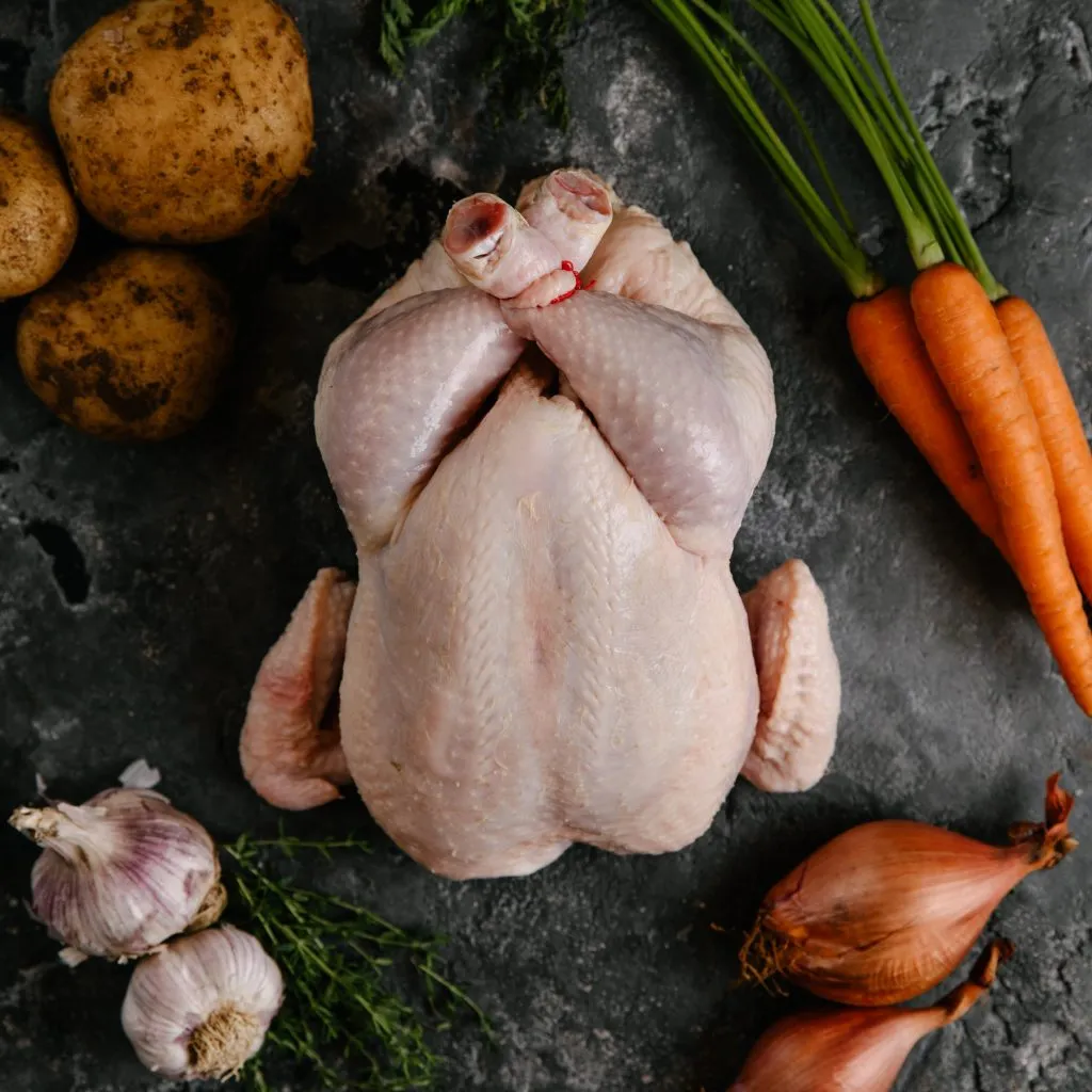 Whole raw chicken with vegetables on a dark surface.