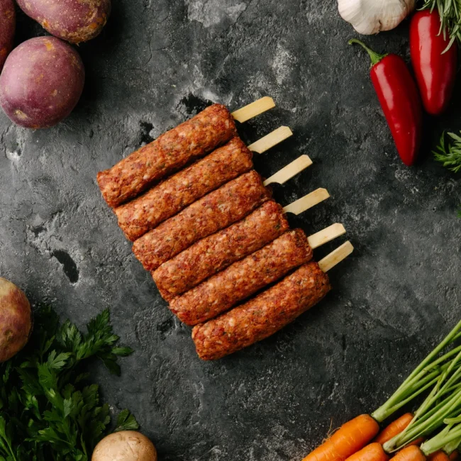 Raw meat kebabs with vegetables on dark background